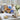 Thinking of You Gift Basket Regular size: a white gift box with navy crinkle, filled with comfort treats including Thinking of You chocolate chip cookies, Dipping Pretzels, Sumatra coffee, a jar of preserves and a tub of trail mix, styled on a whitewashed wooden table by a sunny window with white hydrangeas