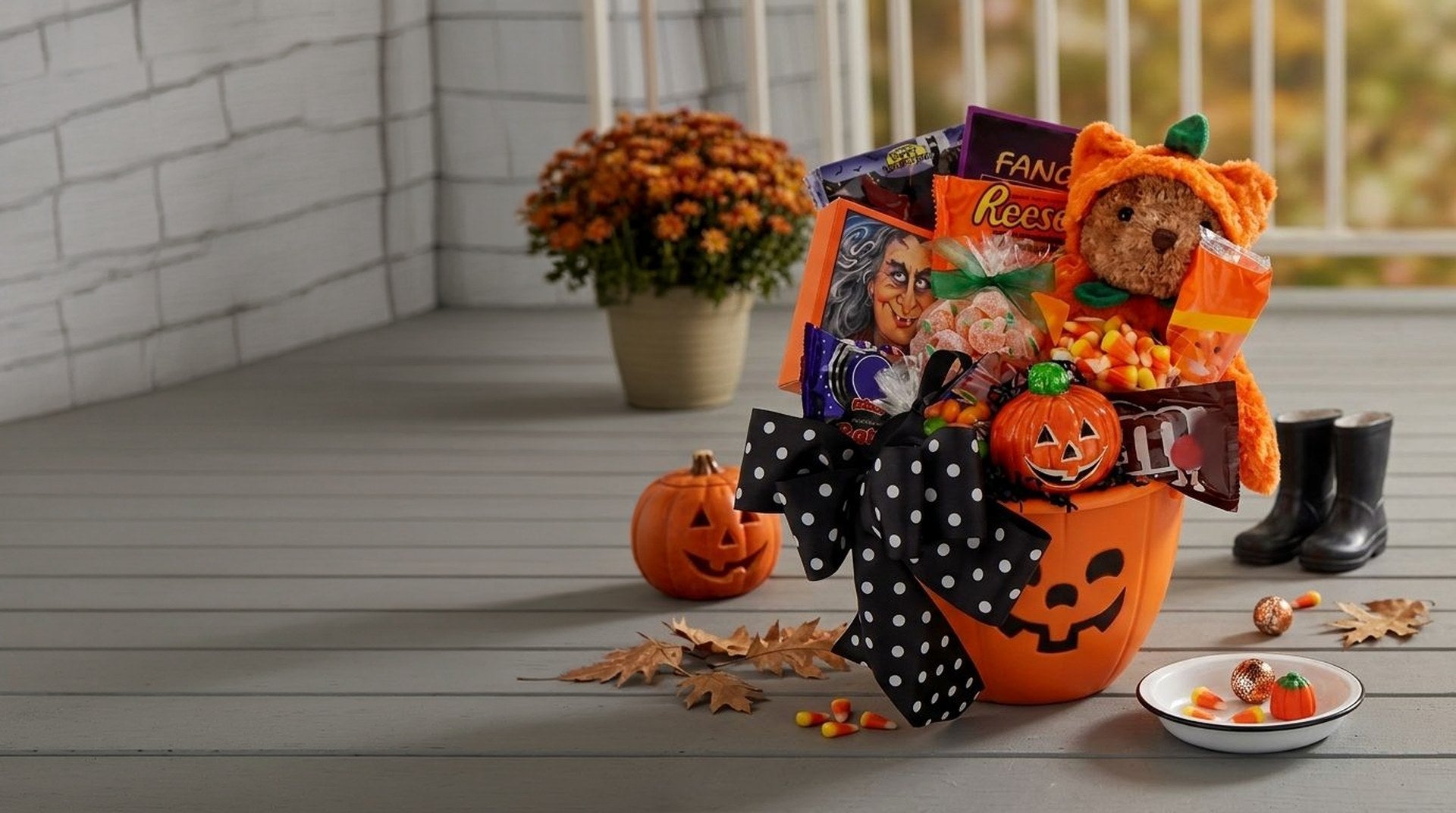 Trick or Treat Halloween Gift Basket, a jack-o-lantern pail of candy with a plush bear in a pumpkin costume, on an autumn porch