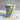 Jar of blue and yellow layered cupcake dessert, wooden spoon, and a customizable 'Hello Baby Boy' label on a marble surface.