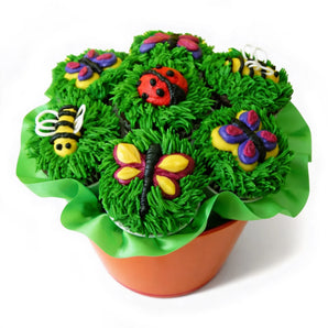 Decorative spring cupcake arrangement in a pot shaped container. The cupcakes have green frosting for grass and colorful nature inspired decorations such as butterflies, bees, and ladybug on them over a white background.