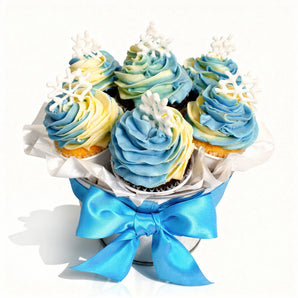 Winter themed bouquet of cupcakes with blue and yellow frosting, decorated with white snowflakes and a blue ribbon on a white background.